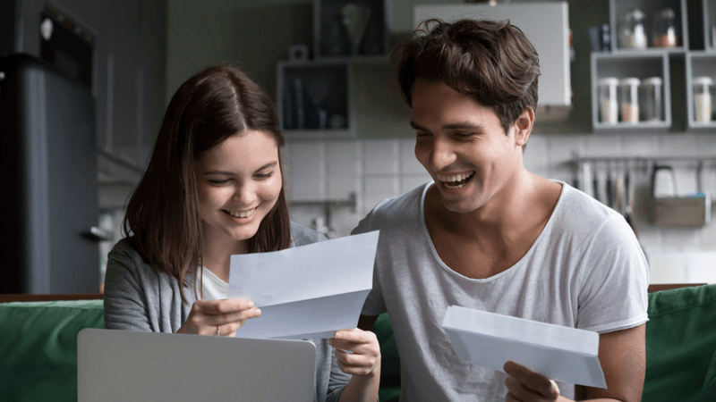 Two young adults reading a document and smiling.