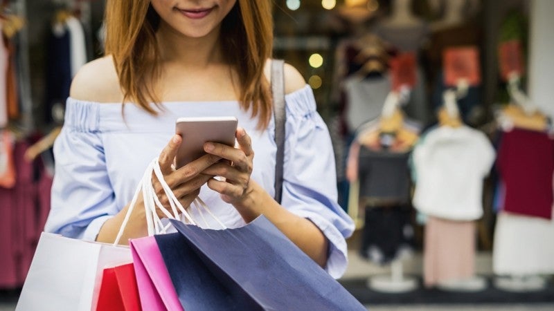 Woman looking at her phone while holding many shopping bags.