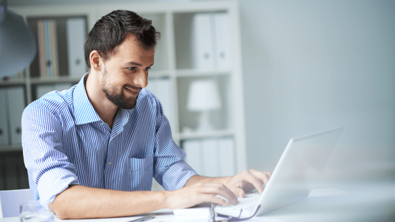 Smiling man typing on a laptop.
