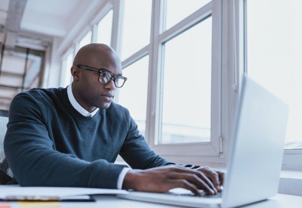 Man wearing glasses typing on a laptop computer.