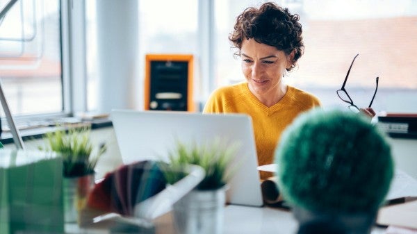 Woman sitting at her desk writing on a paper while looking at her laptop screen.