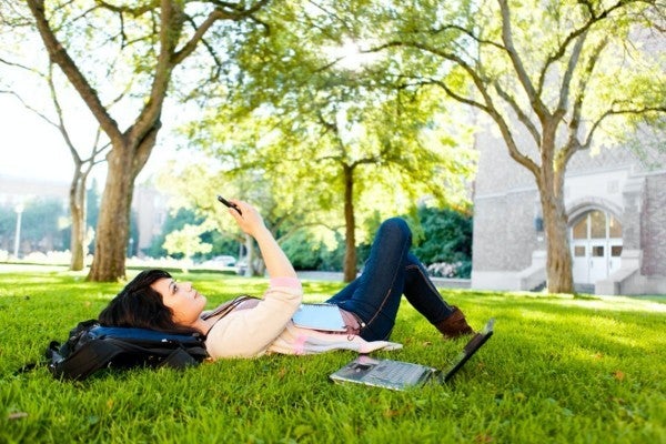 Student laying on the grass filling out a university review with her phone.