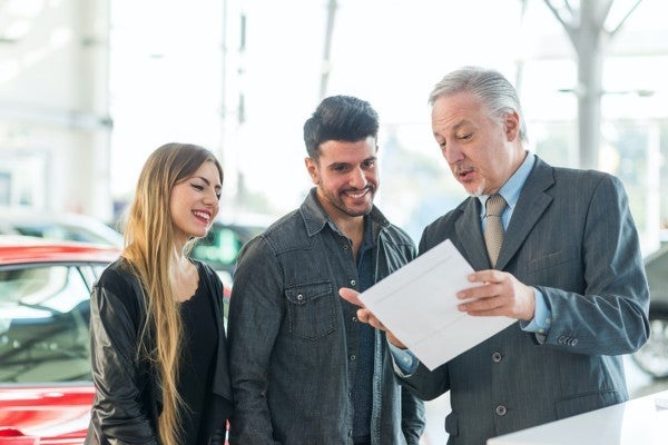 Smiling couple speaking with a car salesman.