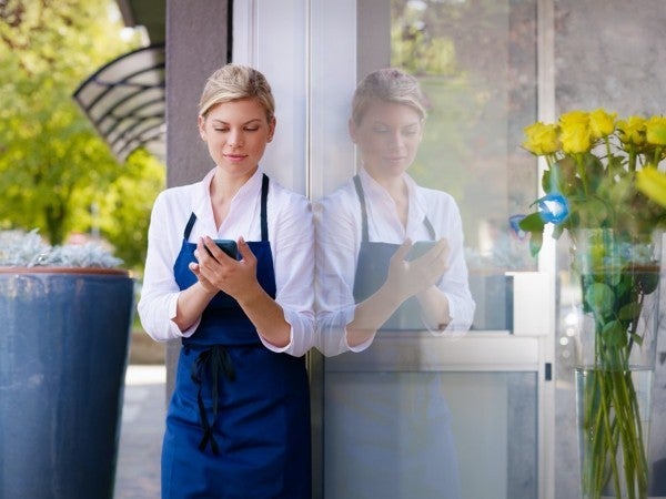 Shop owner standing outside her shop looking at her phone.