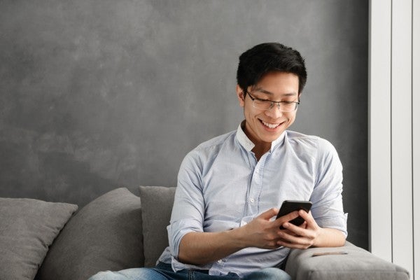 Smiling man sitting while looking at his phone.