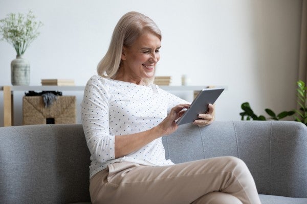 Smiling woman sitting while looking at her tablet.