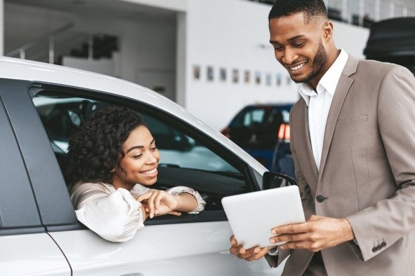 Smiling woman sitting in a new car speaking with a car salesman.
