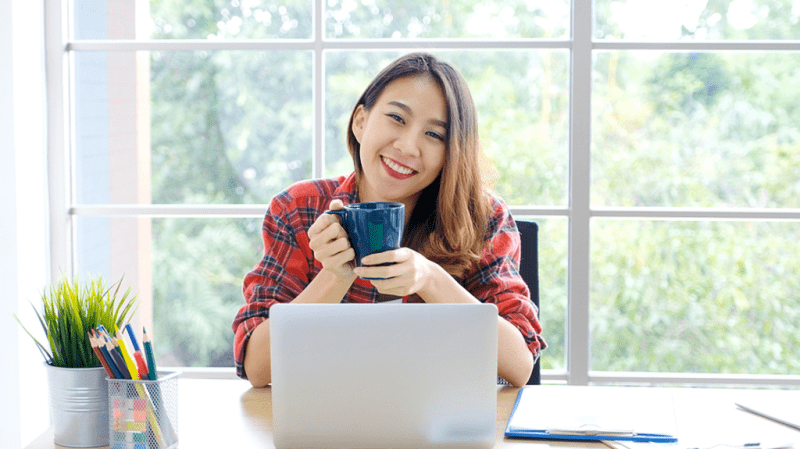 Smiling woman sitting at her desk drinking coffee.