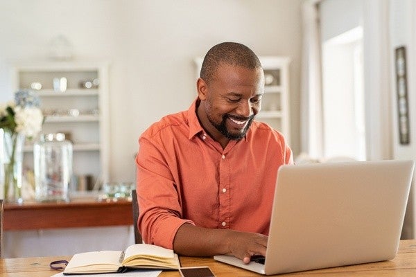 Smiling man reading his social media post using a laptop computer.