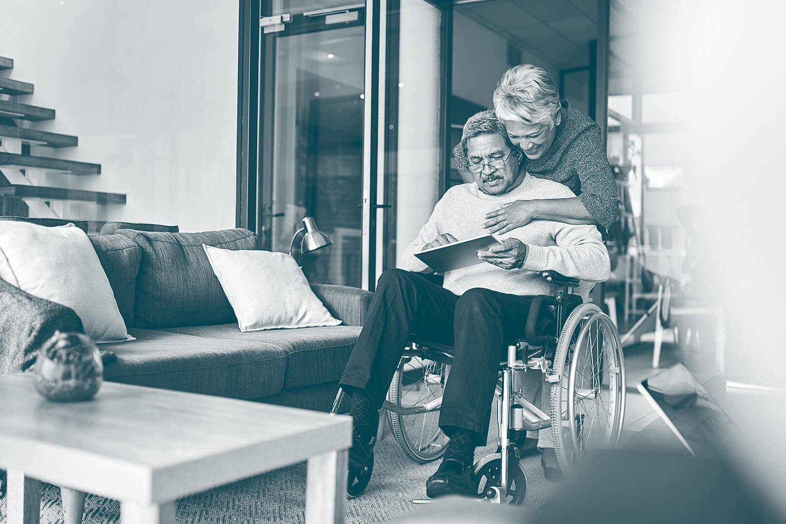 Elderly man in a wheelchair, being embraced by his wife. 