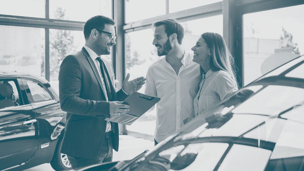 Couple talking to salesman in auto dealer showroom