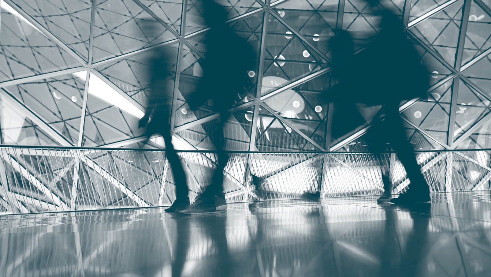 People walking through geometric glass corridor
