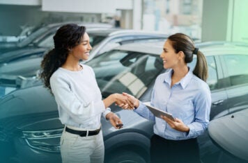 Woman auto salesman shaking hand of female customer.